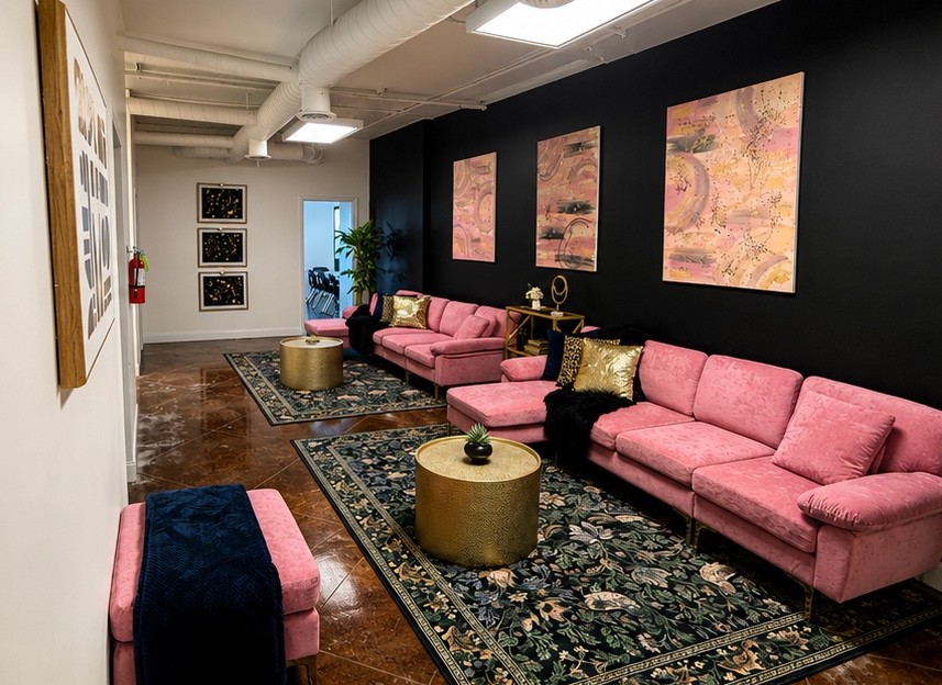 The main lounge at KC Creative Space — pink velvet sofas, gold accent tables, and blush rose gold artwork against a black feature wall